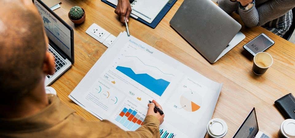 Google Adwords çalışmaları bulunur sarı masanın üstünde bulunan bilgisayar ve insanların  kalemlerinin yanında