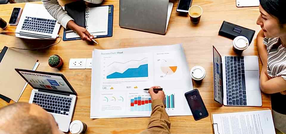 İnternetten para kazanma yolları konuşuluyor masanın üzerinde laptop ve dosyaları olan insanların toplantısında..